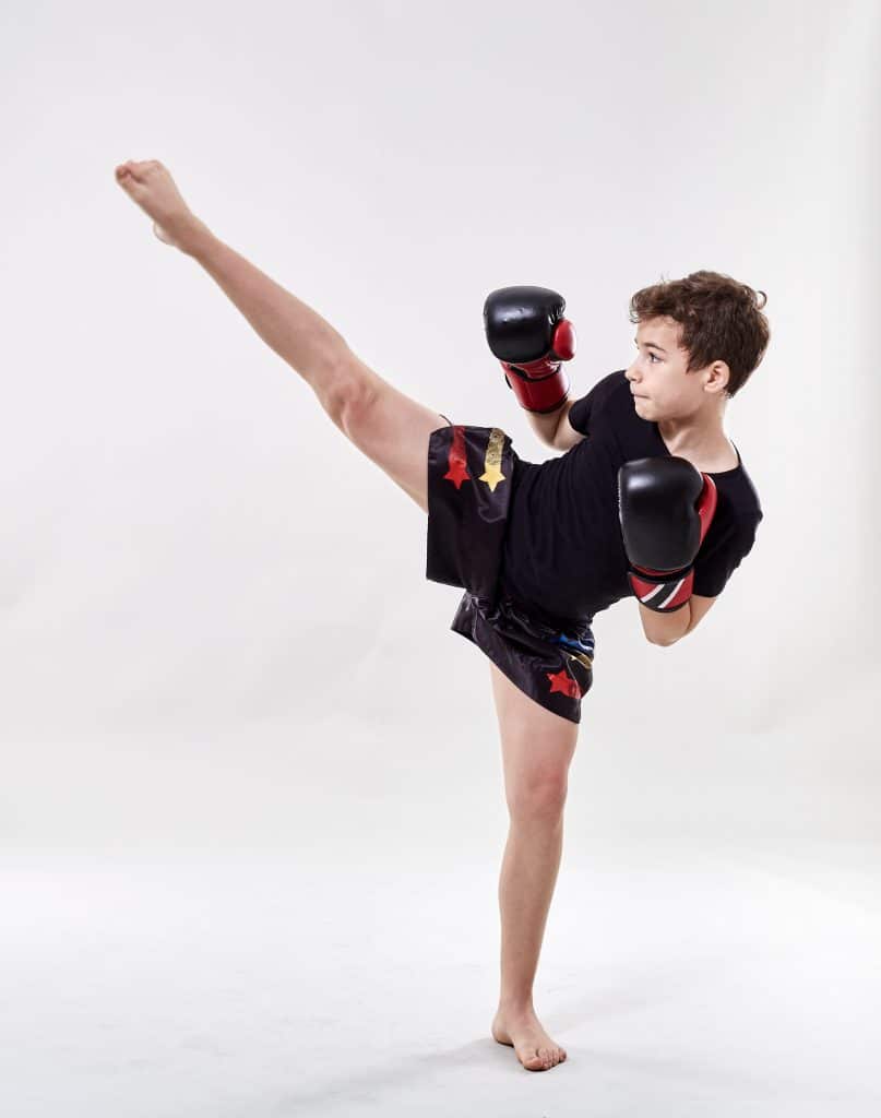 Kinder Kick-Thai-Boxing: Junge mit Boxhandschuhen der seitlich in die Luft tritt